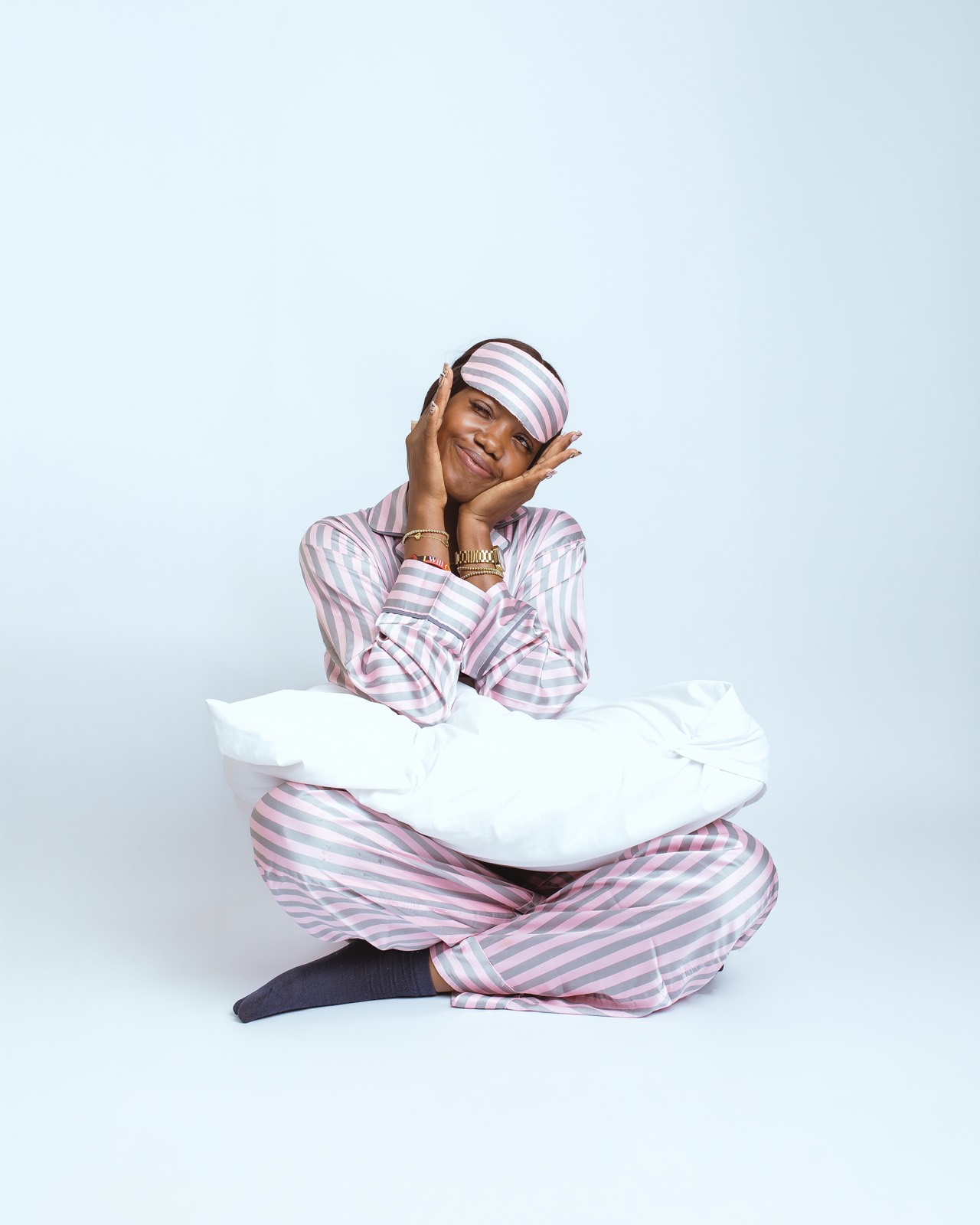 Woman in a blush striped satin pajama set sitting with a white pillow
